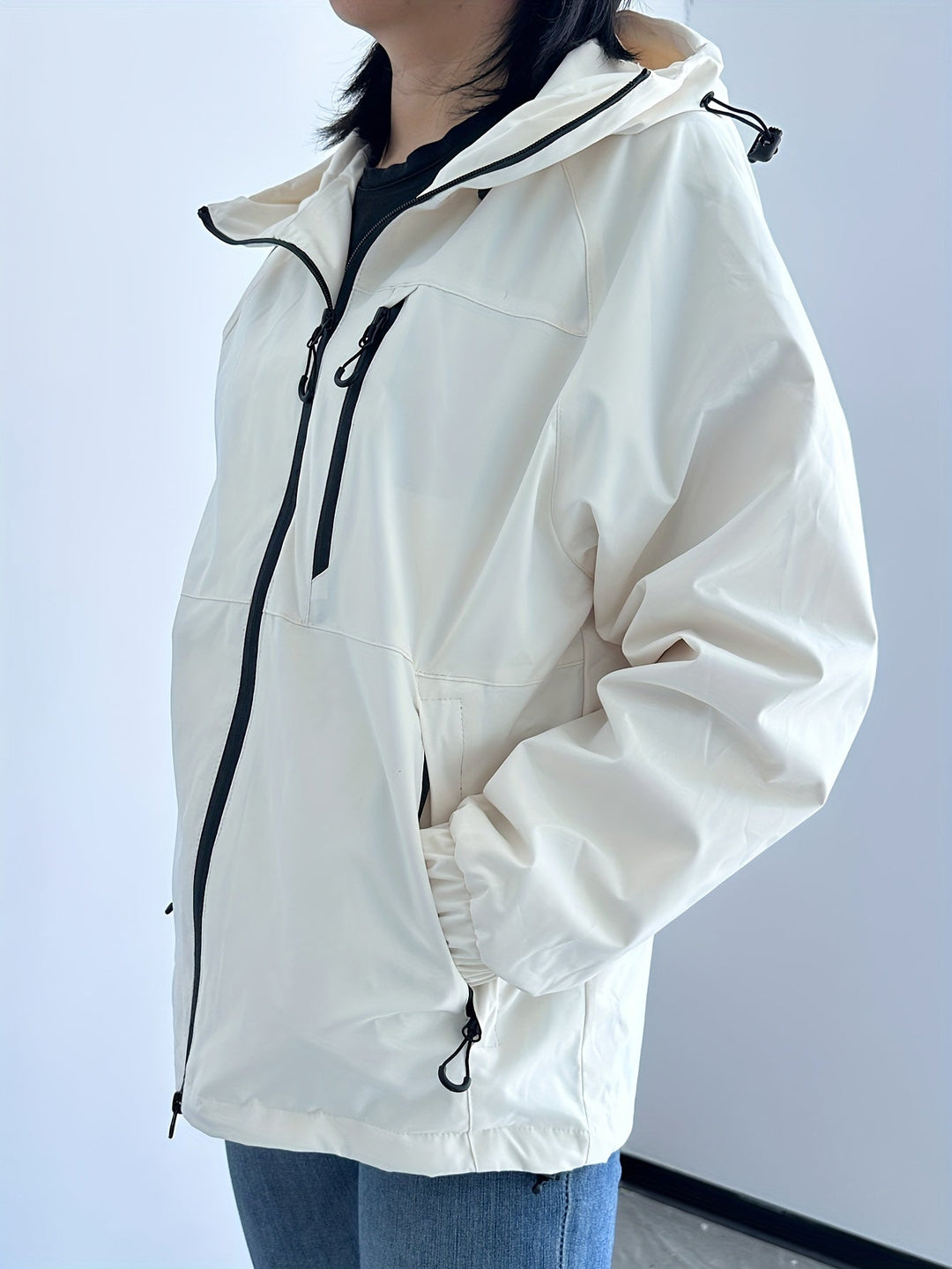 Femme portant une veste imperméable légère à capuche, active en extérieur, protection coupe-vent polyvalente.