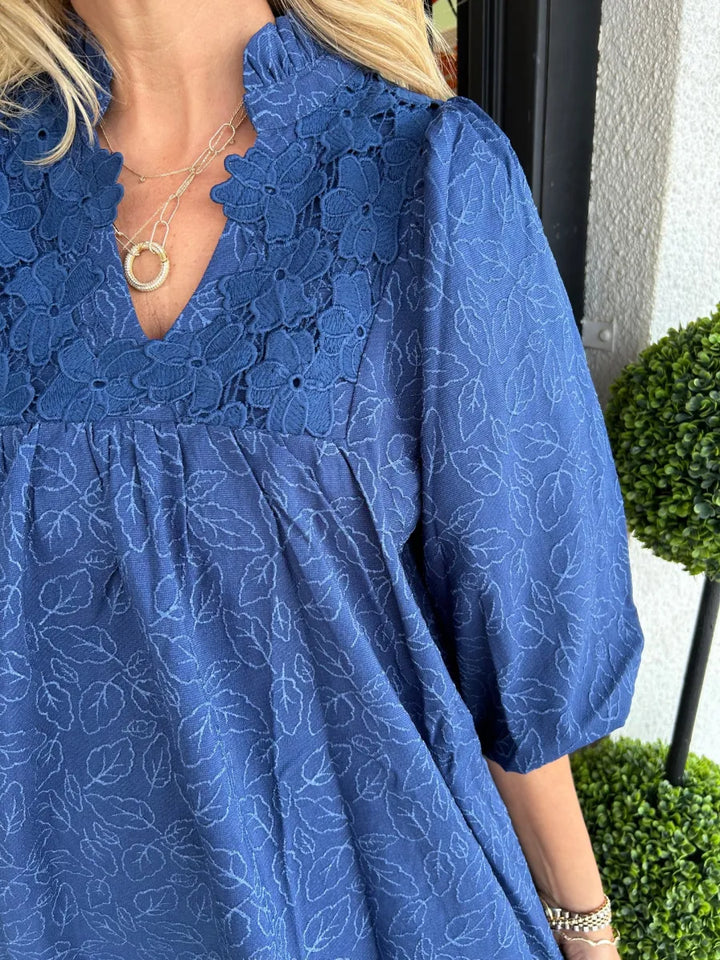 Femme portant une robe courte jacquard élégante, col V, manches bouffantes. Tenue parfaite pour l'été.