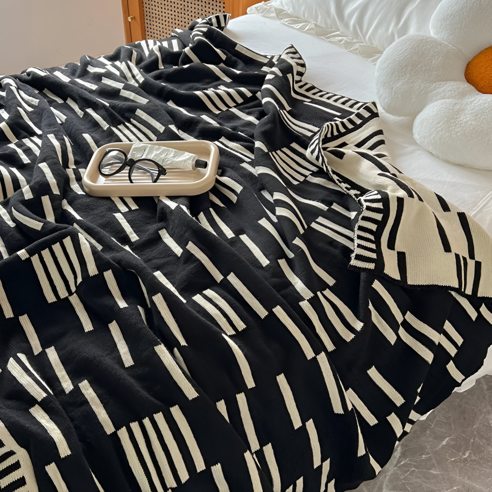 Plaid tricoté en acrylique, motif noir et beige, texture douce et confortable pour toutes saisons.