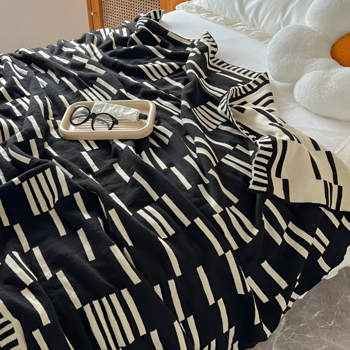 Plaid tricoté en acrylique, motif noir et beige, texture douce et confortable pour toutes saisons.