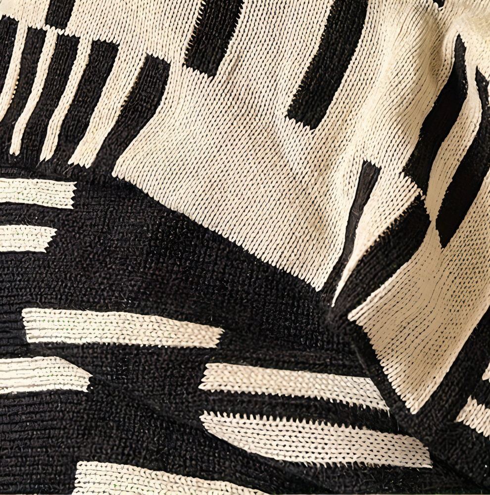 Plaid tricoté noir et beige, aspect doux et confortable, parfait pour ajouter une touche de décoration chaleureuse.