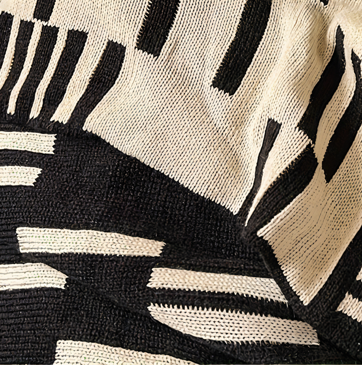 Plaid tricoté noir et beige, aspect doux et confortable, parfait pour ajouter une touche de décoration chaleureuse.