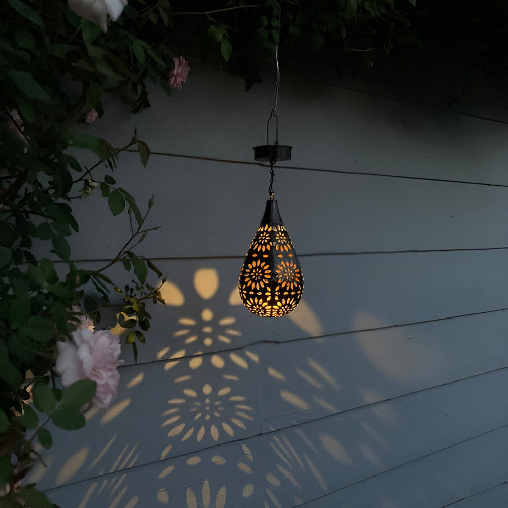 Lanterne solaire de jardin en métal s'illuminant sur une terrasse, créant une ambiance magique la nuit.
