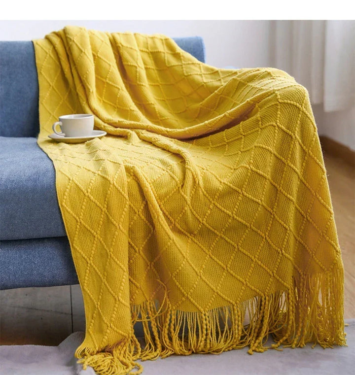 Couverture tricotée beige clair, bohème chic, drapée sur un lit, créant une atmosphère douce et accueillante.