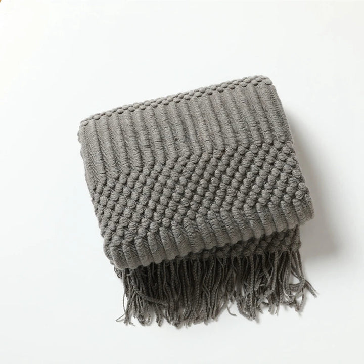Plaid tricoté beige, style bohème, jeté avec désinvolture sur un canapé, pour une déco chic et relax.