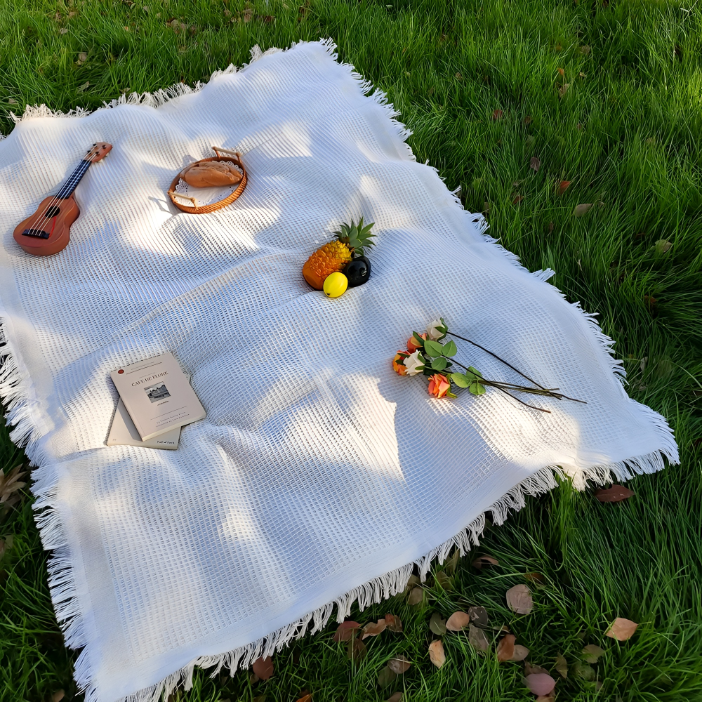 Couverture de pique-nique blanche bohème avec ses pompons décoratifs pour un jardin chic.