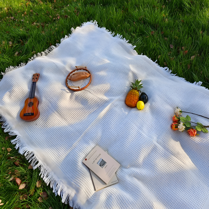 Couverture de pique-nique bohème blanche avec pompons, offrant confort et style pour votre jardin.