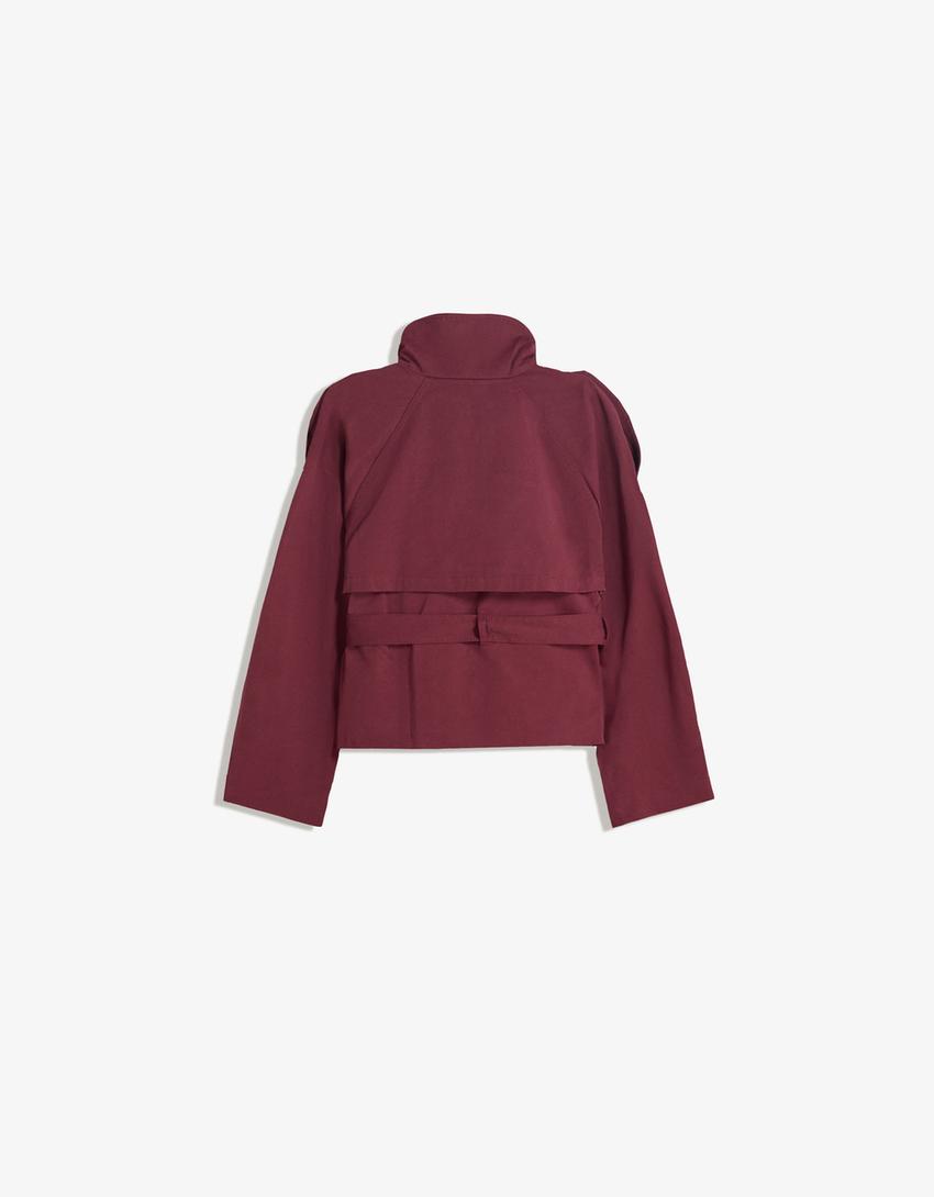 Femme portant un trench court, veste élégante à ceinture, style urbain chic, parfait pour le printemps.