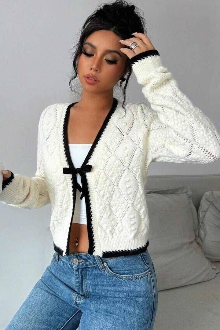 Cardigan femme blanc ajouré avec joli nœud et bordures contrastées. Manches longues, coupe courte, style printanier.