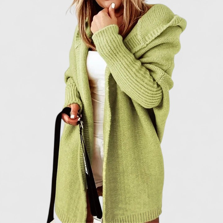 Femme posant avec un cardigan long oversize à capuche, look moderne et décontracté pour l'hiver.