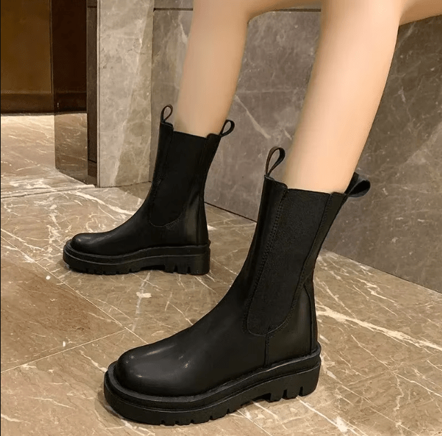 Paire de bottes Chelsea pour femmes en cuir noir, mi-mollet, avec élastique latéral et semelle crantée robuste.
