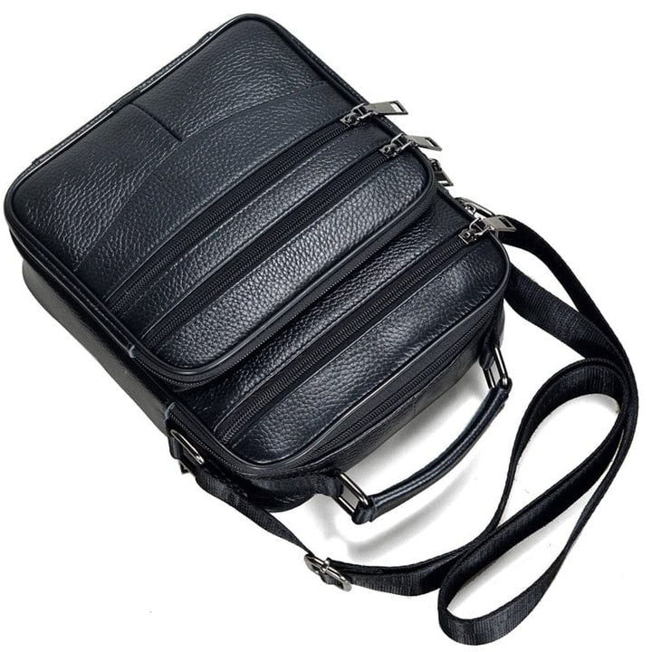 Sac bandoulière en cuir véritable noir, visible de face, avec détails des zips et texture du cuir.
