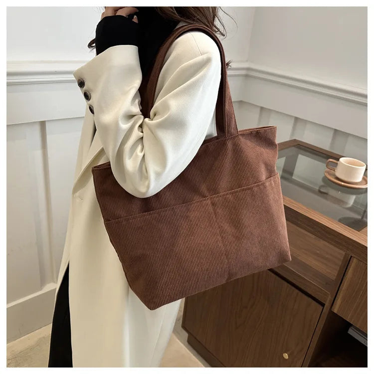Femme portant un sac cabas élégant en velours côtelé, bandoulière, style automne-hiver décontracté.