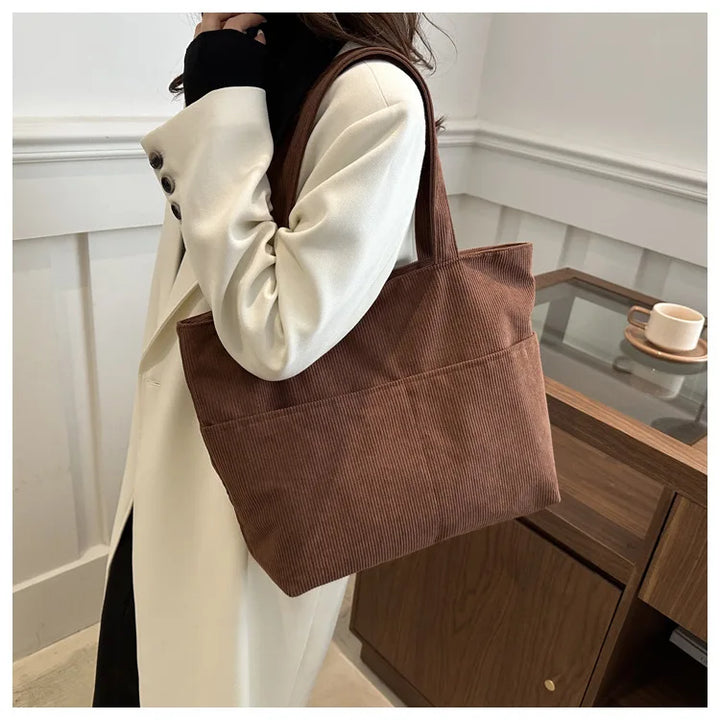 Femme portant un sac cabas élégant en velours côtelé, bandoulière, style automne-hiver décontracté.