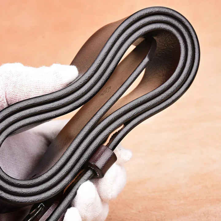 Gros plan sur la texture du cuir de vachette d'une ceinture homme vintage, avec surpiqûres fines et boucle.
