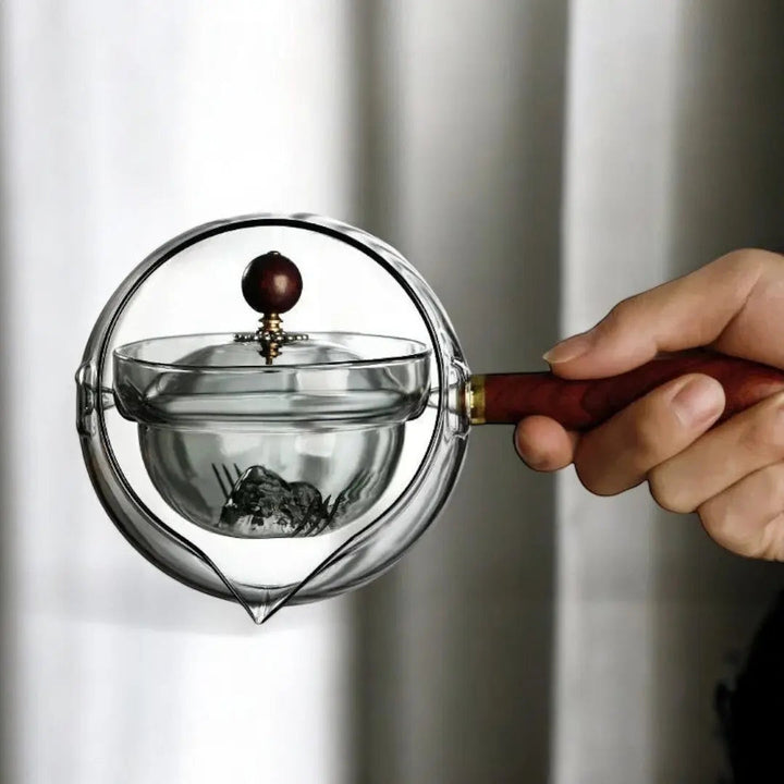 Détail du verre borosilicate résistant et du support en bois élégant de la théière rotative.